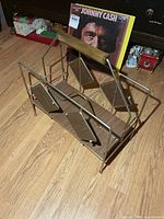 Front angled view of brass-tone metal magazine rack with wood shelf and handle