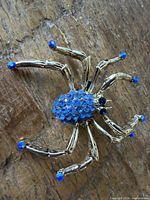 Top view of gold tone spider brooch showing blue rhinestone abdomen and leg tips