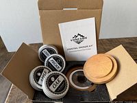 Open box showing wooden lid, mesh diffuser, four wood chip tins and instructions