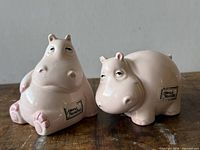 Front view of both ceramic hippo shakers showing poses, color, size and labels
