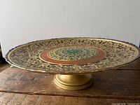 Side view of glass pedestal cake plate showing footed base and ornate surface design