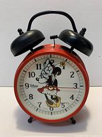 Front view of Minnie Mouse quartz table clock showing dial, twin bells, feet, overall design
