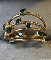 Front view of gold-tone multi-band ring showing green stones and overall design