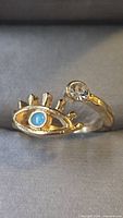 gold-tone open band ring with eye motif and clear stone