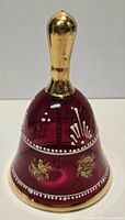 Full view of cranberry glass bell showing gold handle, gilt motifs and enamel dots
