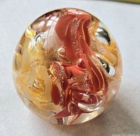 Front view of glass paperweight showing red, orange, yellow swirls and bubbles