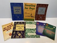 Front covers of nine vintage scouting booklets laid out for identification