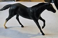 Full left side view of black model horse figurine showing trotting pose and white rear sock