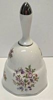 Front view of porcelain bell showing floral decoration and metal finial