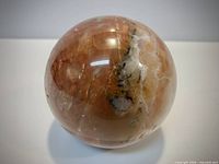 Front view of polished agate sphere showing orange and cream banding with druzy pocket