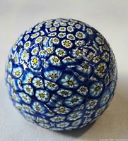 Full view of spherical glass millefiori paperweight showing blue, white, yellow cane pattern