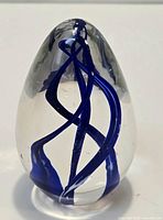 Front view of clear egg-shaped glass paperweight showing blue internal swirls