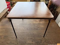 Top view of square card table showing brown vinyl surface and metal edge