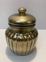 Front view of brass-tone ribbed glass canister with lid