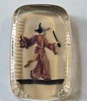 Overall view of glass cabochon paperweight showing needlepoint figure and scalloped edges