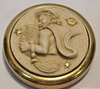 Top view of round brass paperweight with ivory-style relief design