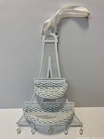 Front view of white metal Eiffel Tower wall organizer showing shelves, hooks and ribbon hanger