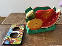 Front view of both items showing painted fruit napkin holder and ceramic outlet cover