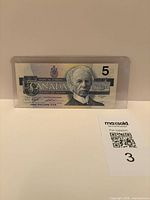 Front of $5 note in protective sleeve showing portrait of Sir Wilfrid Laurier and denomination