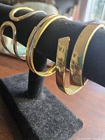 Four bracelets on display stand, focus on three gold-tone cuffs