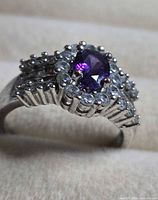 Ring angled view showing purple center stone, halo of clear stones and split shank