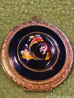 Front view of gold tone locket with enamel floral centre