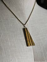 Necklace displayed on mannequin showing gold tone chain and trapezoid tiger’s eye pendant
