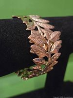 Side view showing gold tone leaf design bracelet on display bar