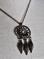 Pendant close-up showing filigree design, centre stone and three leaf dangles