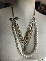 Necklace on mannequin showing layered pearls, chains, and bow