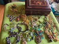Group shot of wooden music box and spread of assorted jewelry on green cloth