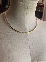 Front view of flat gold-tone collar necklace on mannequin
