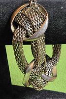 Full view of bracelet hanging on display, showing woven mesh and crossover bars