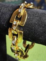 Gold-tone thick link bracelet displayed on stand, showing rhinestone-set links