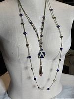 Full view of necklace on mannequin torso showing triple strands, blue beads, rhinestone pendant, and gold-tone drop