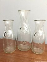 Front view of three clear glass carafes showing size difference and embossed seal