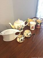 Group shot: both teapots, cream & sugar set, four mugs and tongs on table