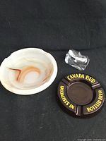 Three smoking accessories: brown Canada Bud ashtray, alabaster ashtray, clear glass pipe holder