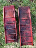 Top view of both red steel car ramps showing ribbed platforms and wear