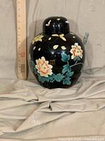 Full view of black floral ginger jar beside ruler showing approx 10 in height