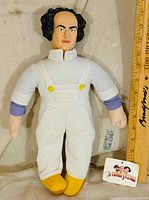 Front view of Larry Fine plush doll showing outfit, facial details, hang tag and size reference ruler