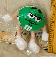 Front view of sealed Green M&M ornament showing facial detail, limbs, packaging