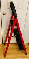 Full side view of folded 4-step ladder showing red frame and black steps