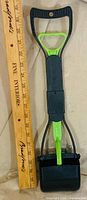 Full view of pooper scooper beside ruler for scale