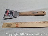 Full view of paint scraper next to ruler for scale