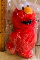 Front view of sealed Tickle Me Elmo plush next to ruler showing height
