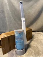 Full view of toilet cleaner brush standing in holder beside shipping box