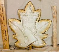 front view of plaster maple leaf plaque with Queen Elizabeth II profile and gold edging, rulers for scale