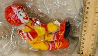 Front view of Ronald McDonald plush in plastic next to ruler for scale