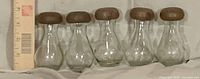 Five clear glass jars with brown lids lined up beside ruler
